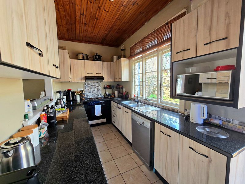 A functional kitchen featuring granite countertops, light wood-finish cabinetry, a double sink, and a timber-clad ceiling with ample natural light.