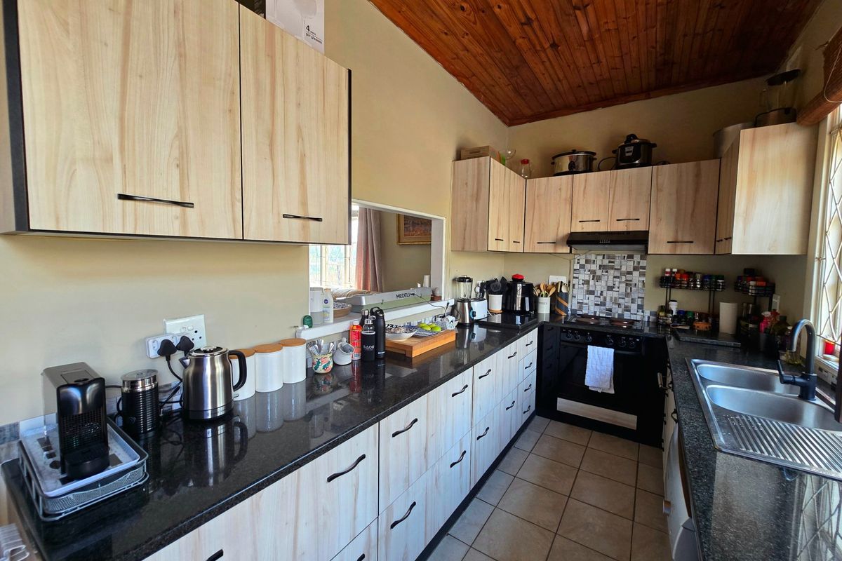 Functional kitchen featuring light wood-look cabinetry, dark granite countertops, a built-in oven with extractor, and a warm timber-paneled ceiling.