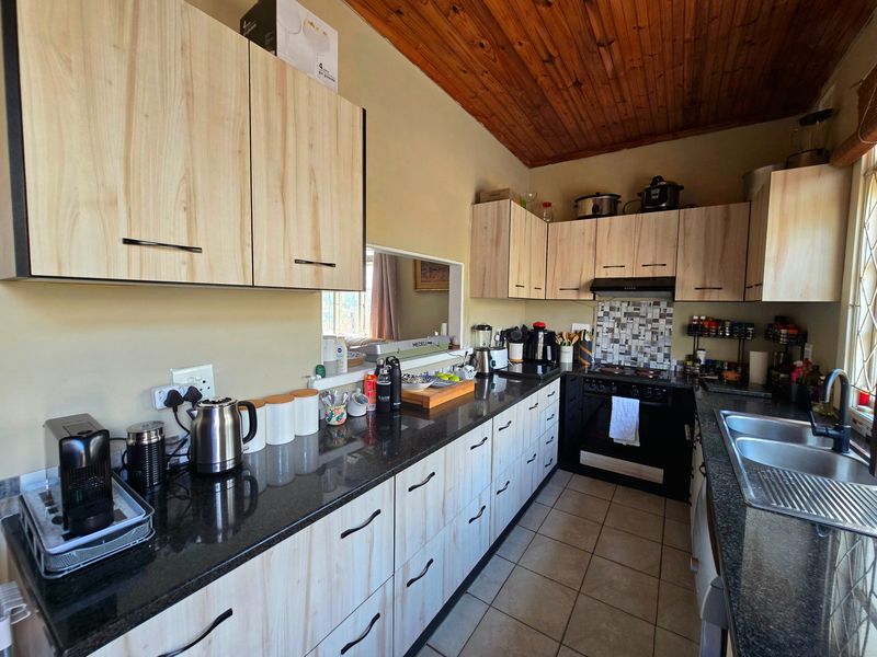 Functional kitchen featuring light wood-look cabinetry, dark granite countertops, a built-in oven with extractor, and a warm timber-paneled ceiling.