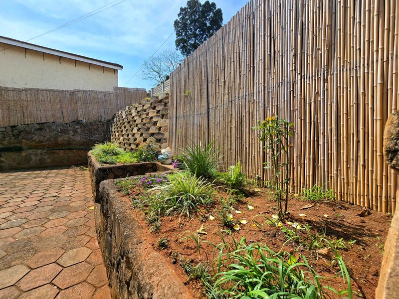 A landscaped garden area featuring raised stone garden beds, paved patio flooring, and bamboo privacy fencing.