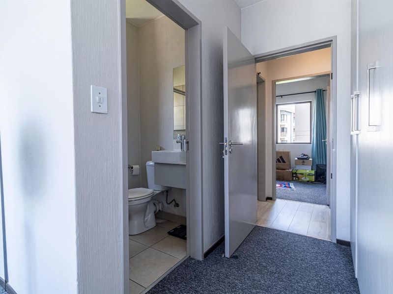 A view from the hallway looking into a compact bathroom and an adjacent bedroom with neutral finishes and functional layout.