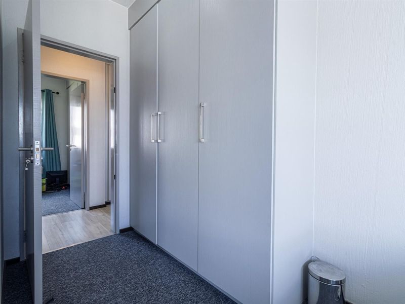 A clean hallway featuring built-in cupboards and carpeted flooring, providing access to adjacent rooms within the apartment.