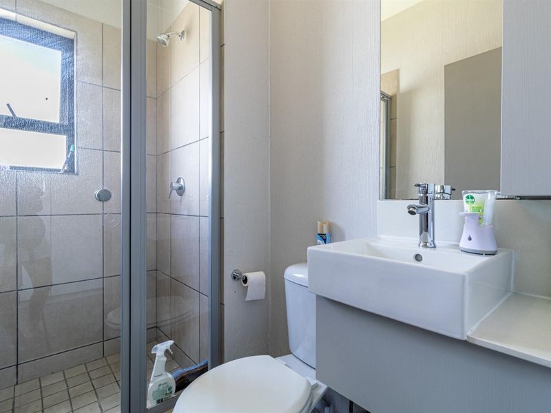 A functional bathroom featuring a glass-enclosed shower, a modern vanity basin with a mixer tap, and a wall-mounted mirror.