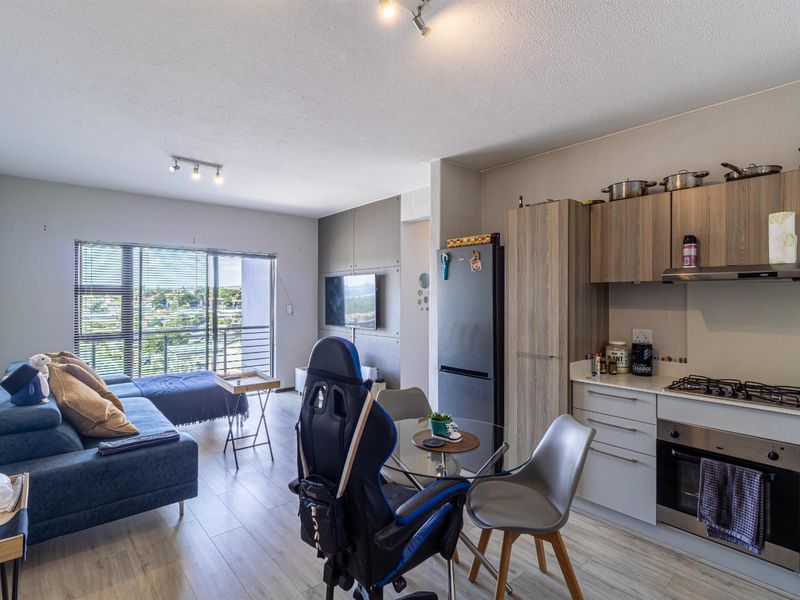 Open-plan living area featuring a modern kitchen with built-in appliances, laminate flooring, and a sliding door leading to a balcony with views.