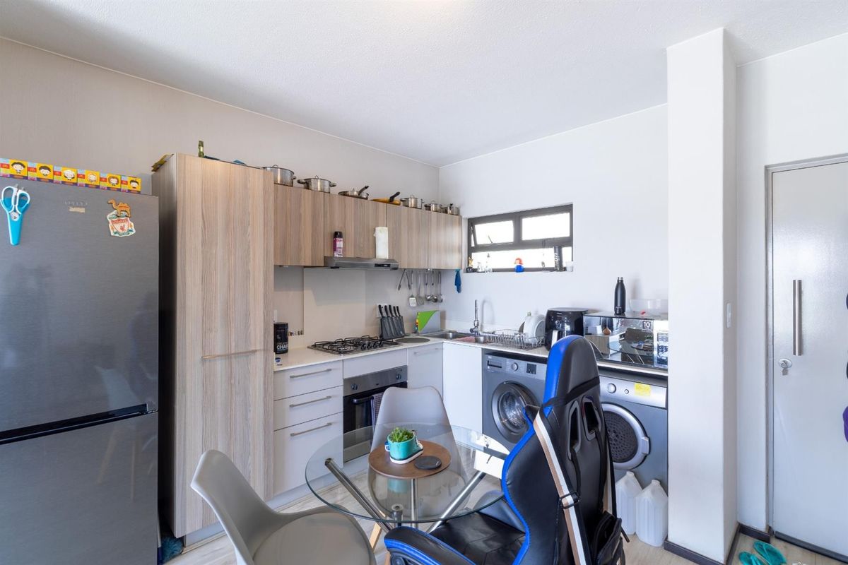 Compact kitchen featuring light wood-finish cabinetry, gas hob, built-in oven, and integrated laundry facilities, providing a functional and efficient workspace.