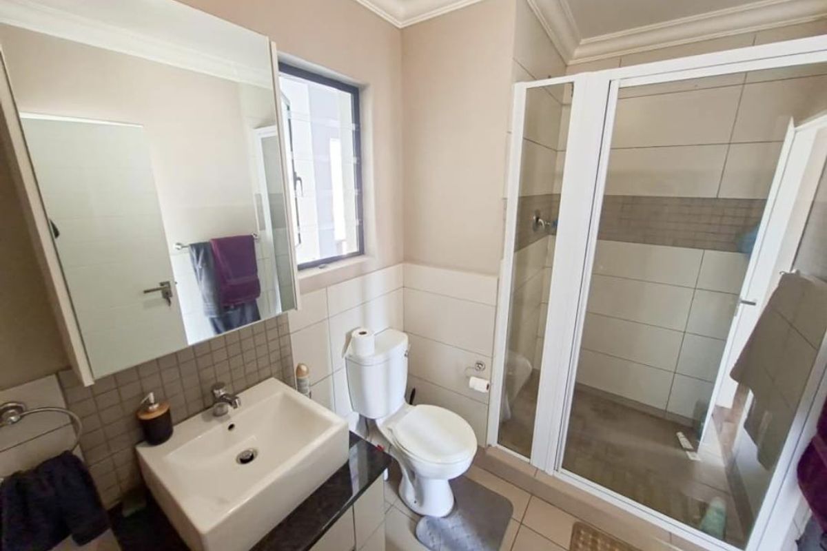 A functional bathroom featuring a shower enclosure, vanity basin, toilet, and wall-mounted mirror cabinet with neutral tiled finishes.