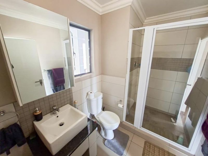 A functional bathroom featuring a shower enclosure, vanity basin, toilet, and wall-mounted mirror cabinet with neutral tiled finishes.