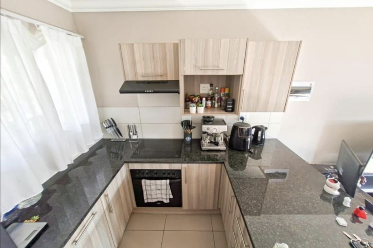 Compact kitchen featuring light wood-look cabinetry, dark granite countertops, built-in oven, electric hob, and an extractor fan with tiled backsplash.