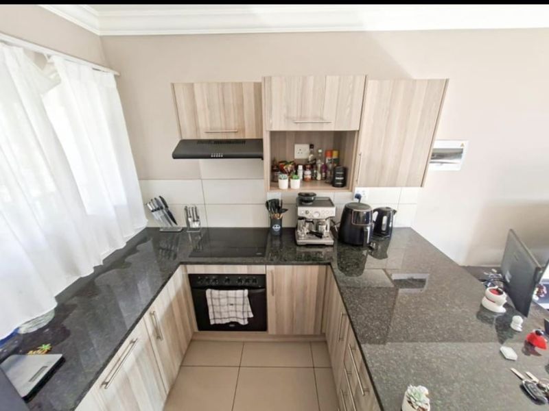 Compact kitchen featuring light wood-look cabinetry, dark granite countertops, built-in oven, electric hob, and an extractor fan with tiled backsplash.