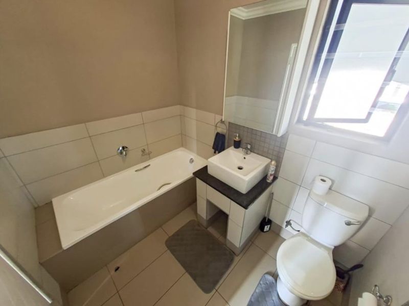 A functional bathroom featuring a built-in bathtub, a modern vanity basin, a toilet, and neutral wall tiling.