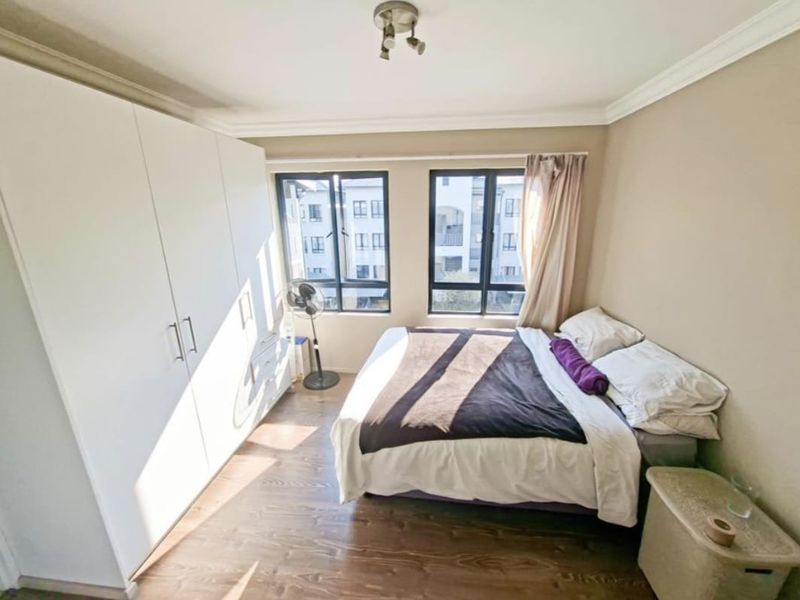 A well-lit bedroom featuring laminate flooring, a large built-in wardrobe, and aluminium-framed windows providing natural light.