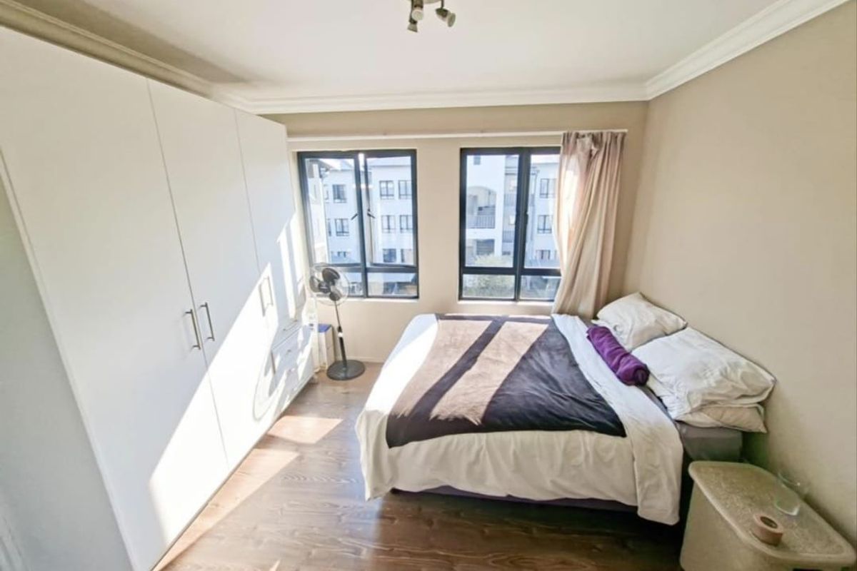 A well-lit bedroom featuring laminate flooring, a large built-in wardrobe, and aluminium-framed windows providing natural light.