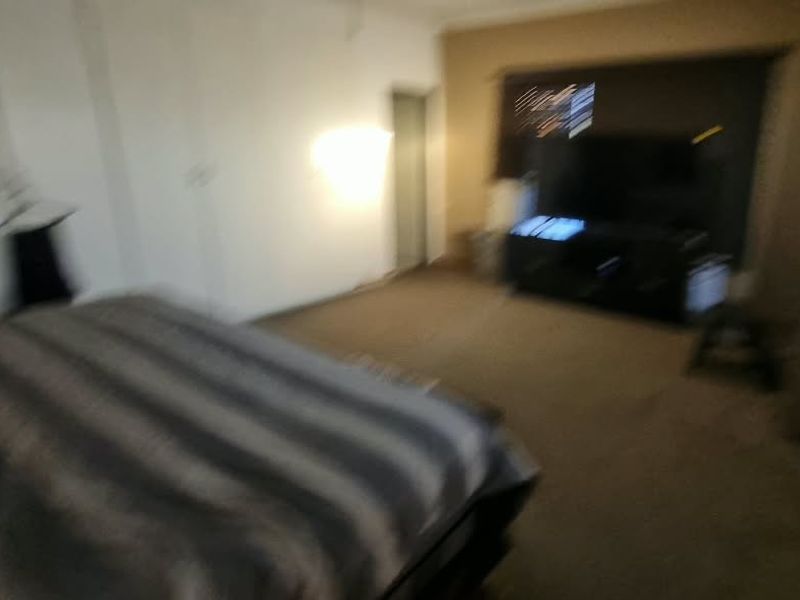 A bedroom featuring carpeted flooring and window blinds, currently furnished with a bed and media console.