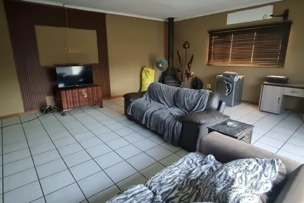 Spacious living area featuring tiled flooring, a wood-burning fireplace, and timber wall paneling, offering a functional layout with natural light through venetian blinds.