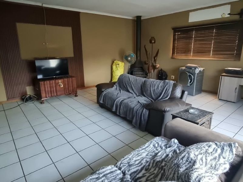 Spacious living area featuring tiled flooring, a wood-burning fireplace, and timber wall paneling, offering a functional layout with natural light through venetian blinds.