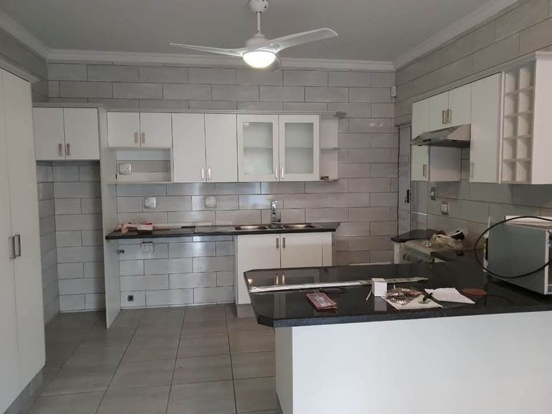 A clean, modern kitchen featuring white cabinetry, granite countertops, a double sink, and a tiled backsplash, offering a functional and bright workspace.