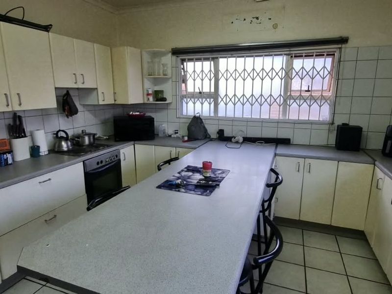 A dated kitchen featuring extensive built-in cabinetry, laminate countertops, a built-in oven, and a tiled backsplash with a window security gate.