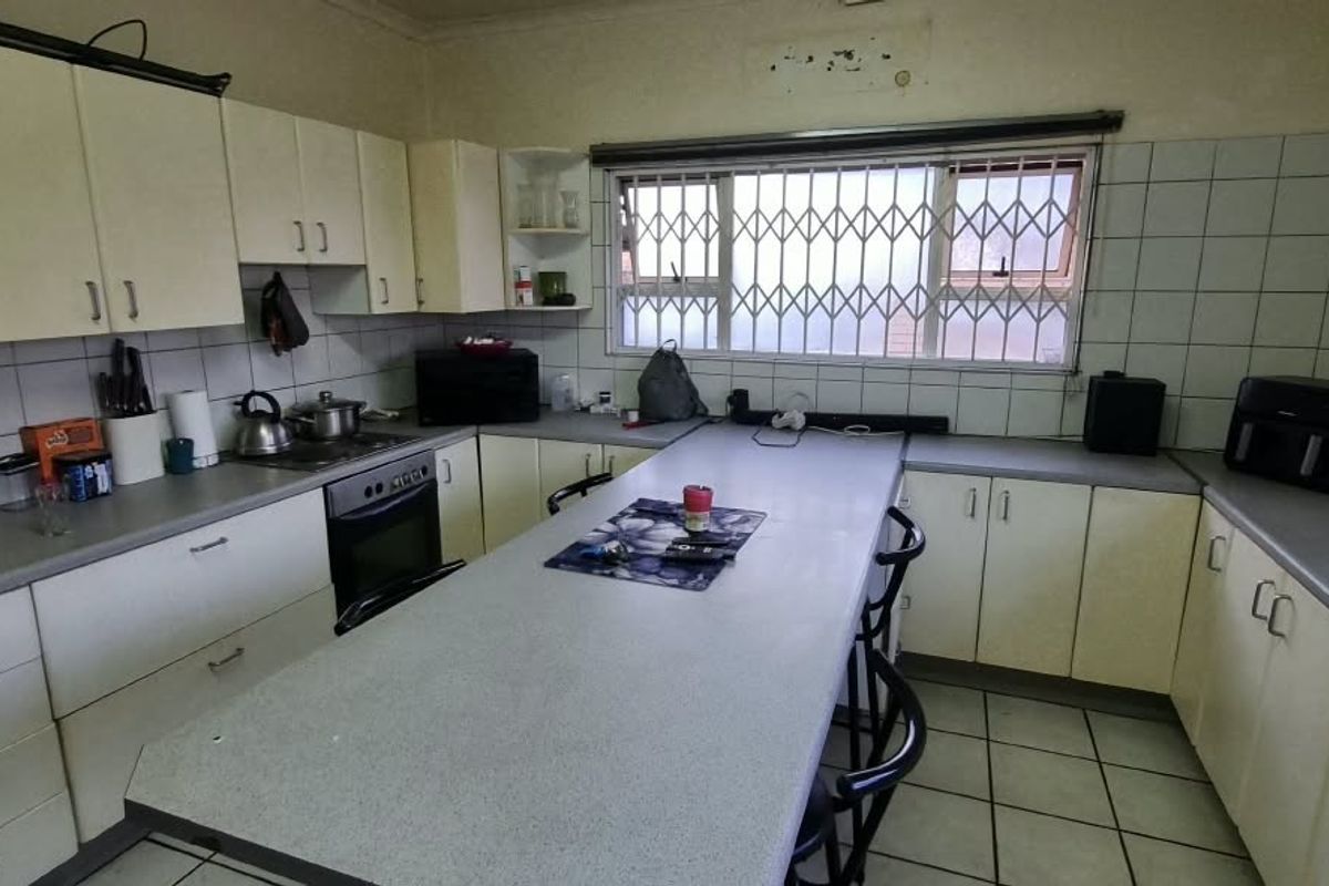 A dated kitchen featuring extensive built-in cabinetry, laminate countertops, a built-in oven, and a tiled backsplash with a window security gate.