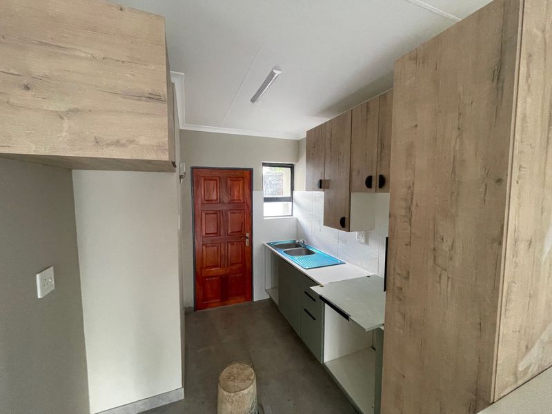 A compact kitchen area featuring light wood-look cabinetry, a double bowl sink, and tiled splashback, currently in need of finishing touches.