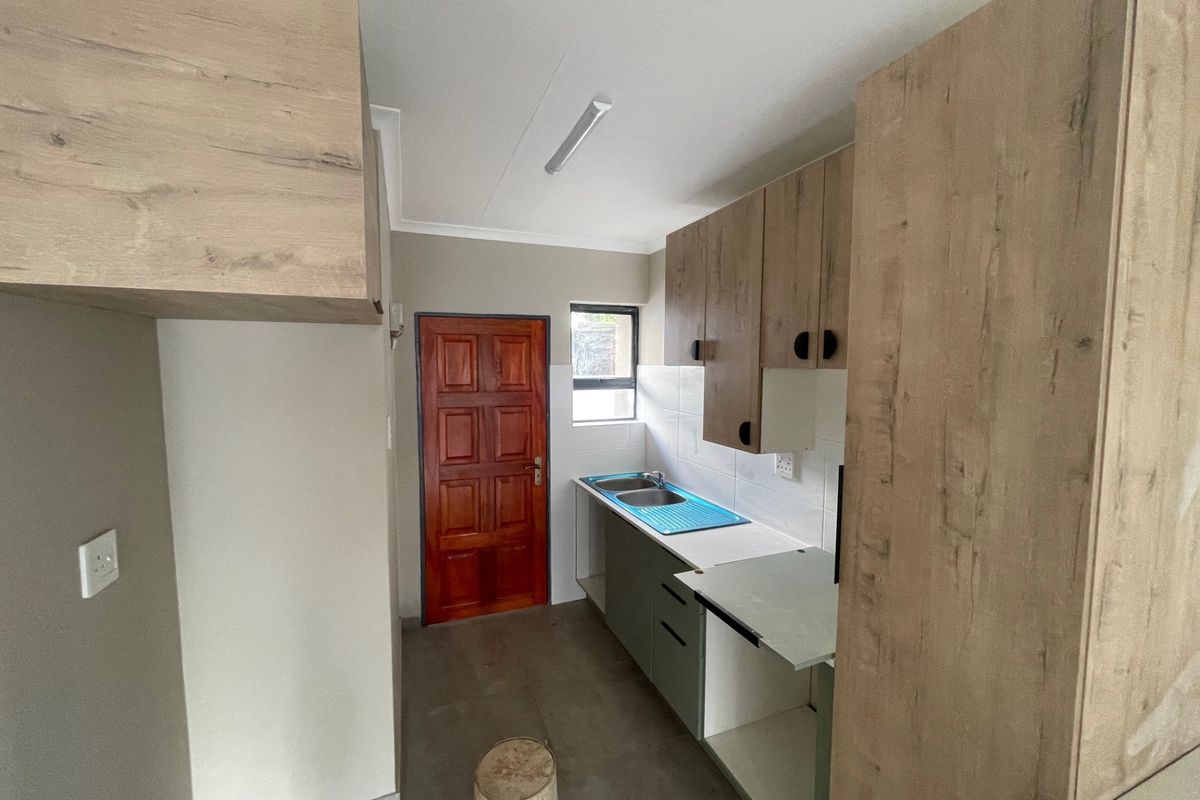 A compact kitchen area featuring light wood-look cabinetry, a double bowl sink, and tiled splashback, currently in need of finishing touches.