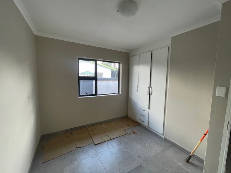 A vacant bedroom featuring neutral wall paint, tiled flooring, and a built-in wardrobe with integrated drawers.