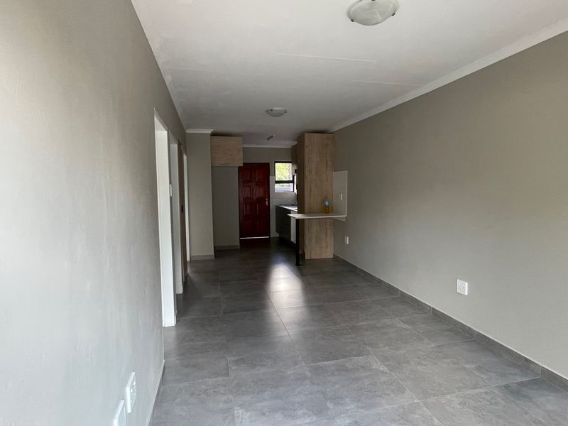 An open-plan living and kitchen area featuring neutral wall tones, modern grey floor tiles, and built-in cabinetry with a breakfast counter.