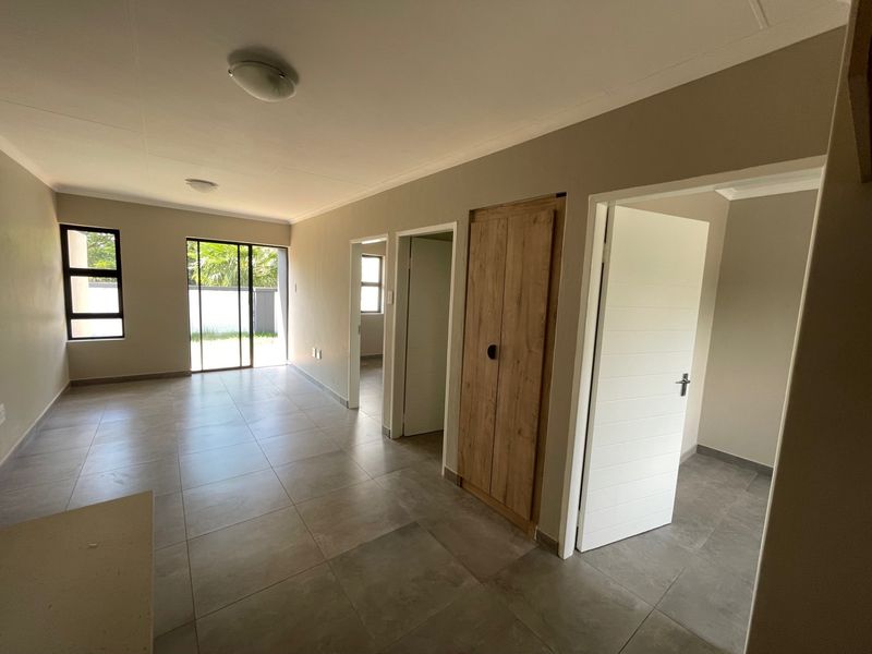 Spacious open-plan living area featuring neutral tiled flooring, modern built-in cabinetry, and direct access to the outdoor space through sliding glass doors.