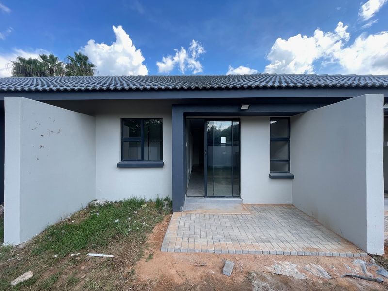 Rear view of a townhouse featuring a paved patio, sliding glass door access, and modern dark-framed aluminium windows under a tiled roof.