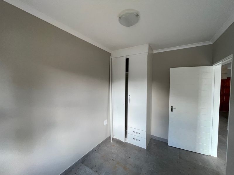 A clean, empty bedroom featuring neutral wall paint, tiled flooring, and a white built-in wardrobe with integrated drawers.