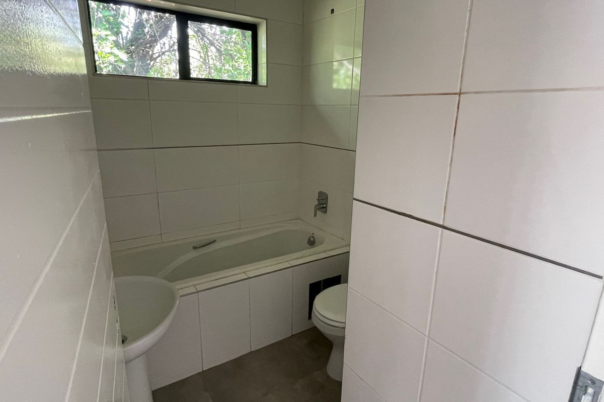 A compact bathroom featuring a bathtub, pedestal basin, and toilet with white wall tiling and neutral floor tiles.