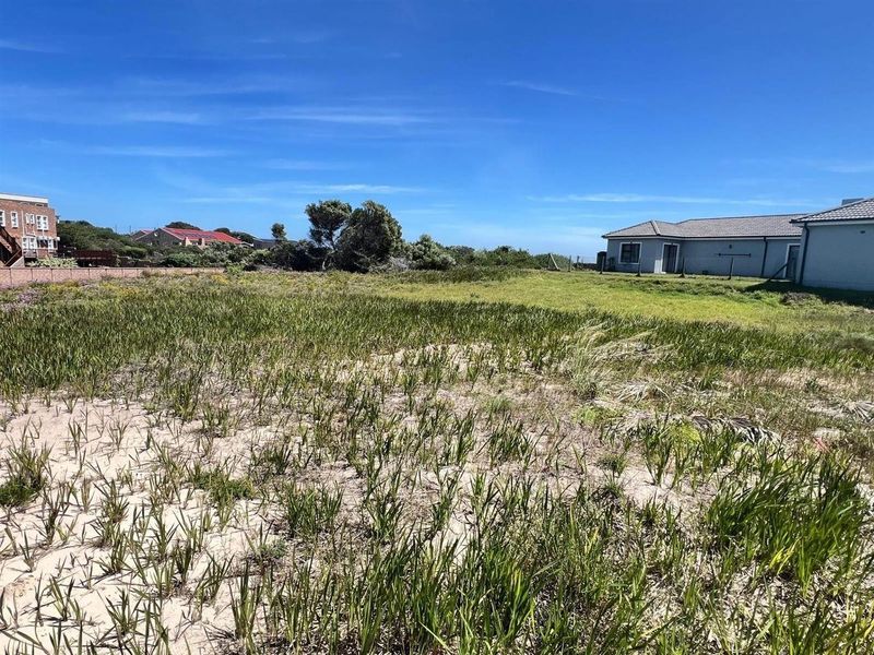 A vacant residential plot featuring natural coastal vegetation, bordered by existing residential properties and fencing.