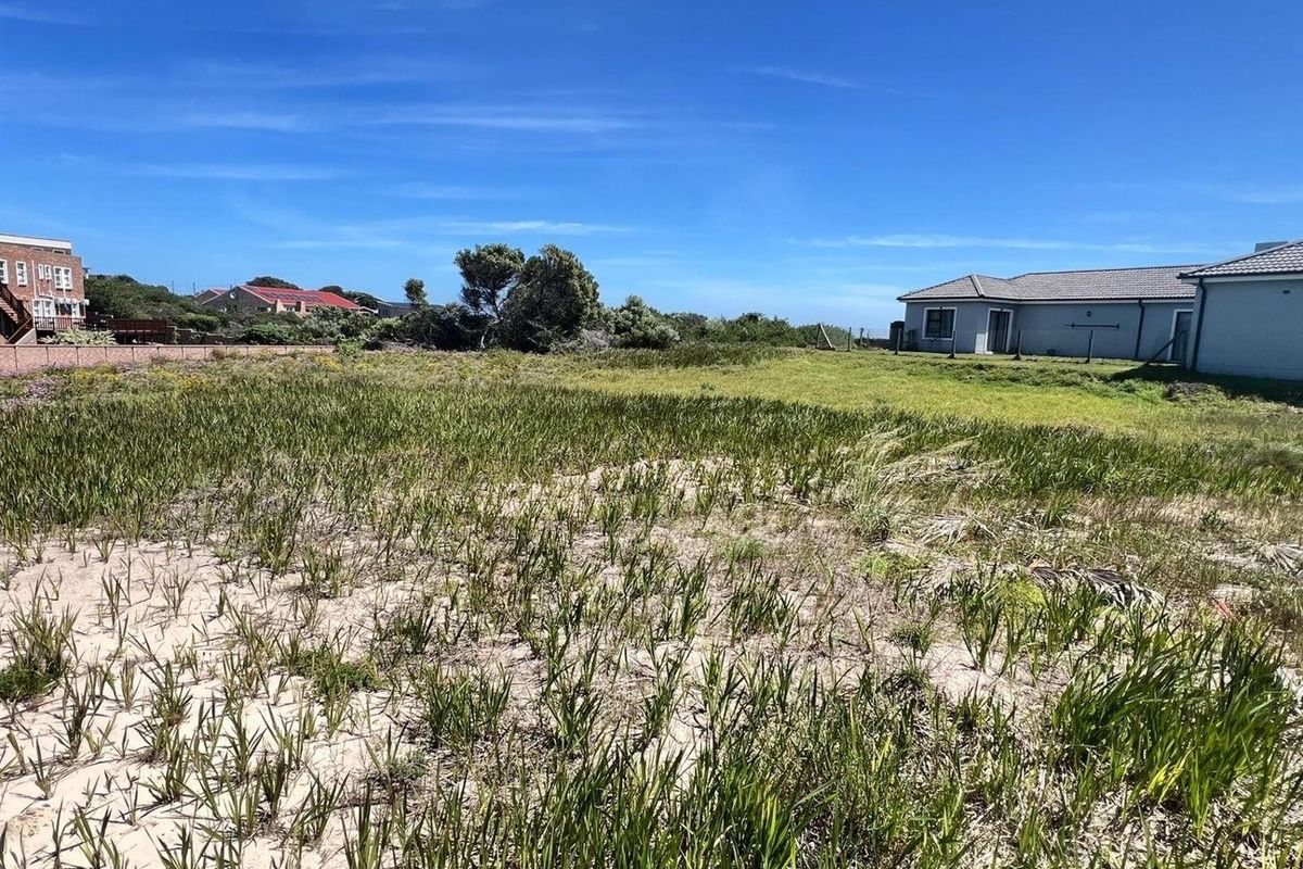 A vacant residential plot featuring natural coastal vegetation, bordered by existing residential properties and fencing.