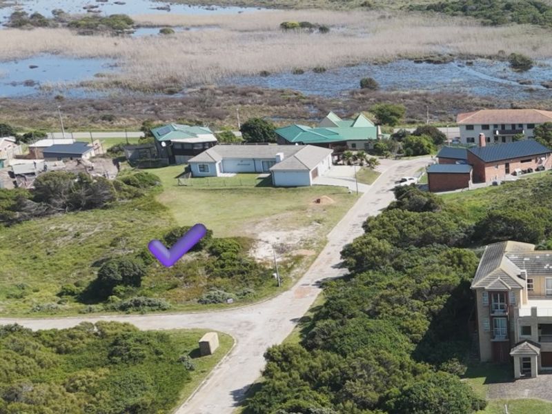 Aerial view of a vacant residential plot situated in a coastal neighborhood with established road access and surrounding natural vegetation.
