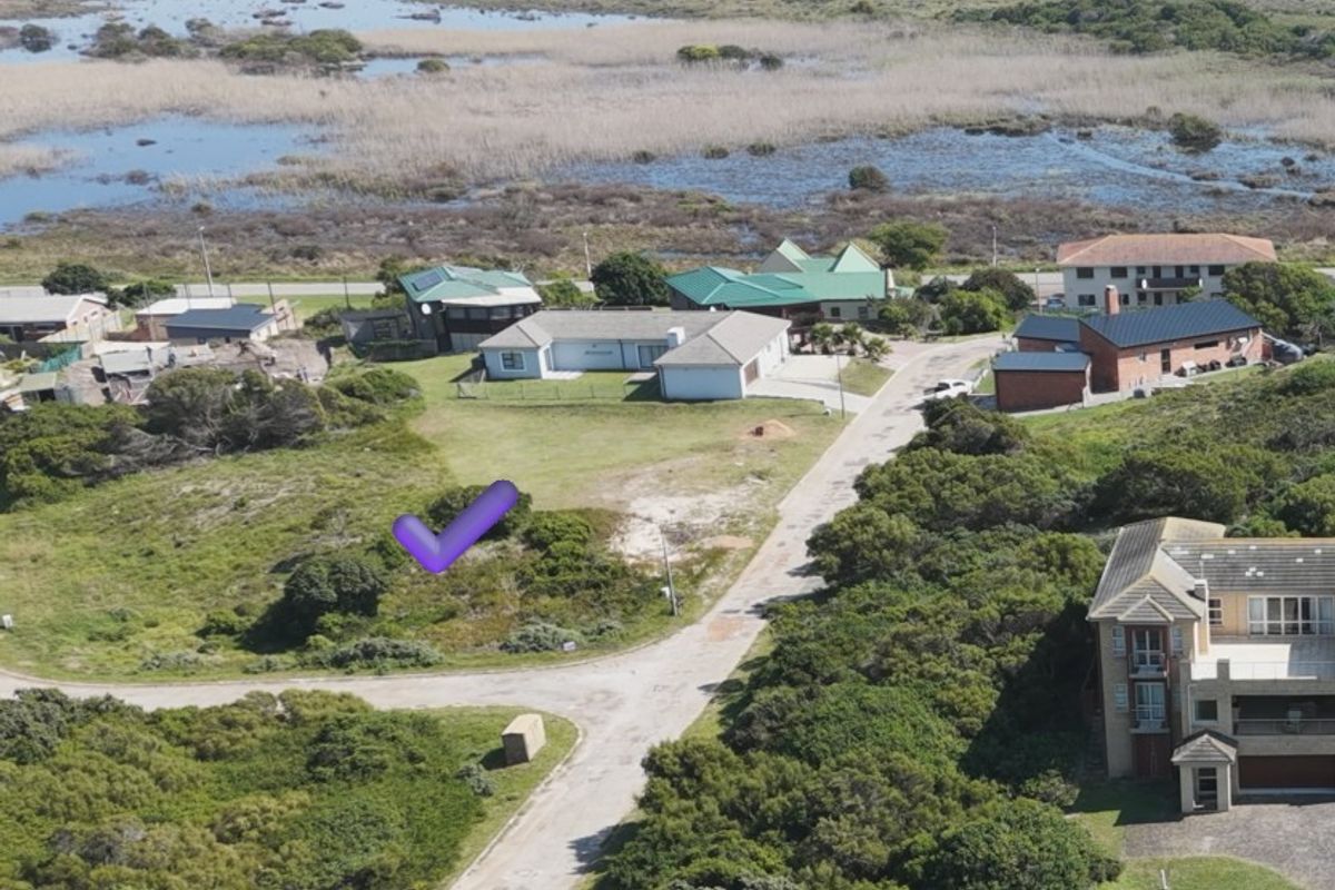 Aerial view of a vacant residential plot situated in a coastal neighborhood with established road access and surrounding natural vegetation.