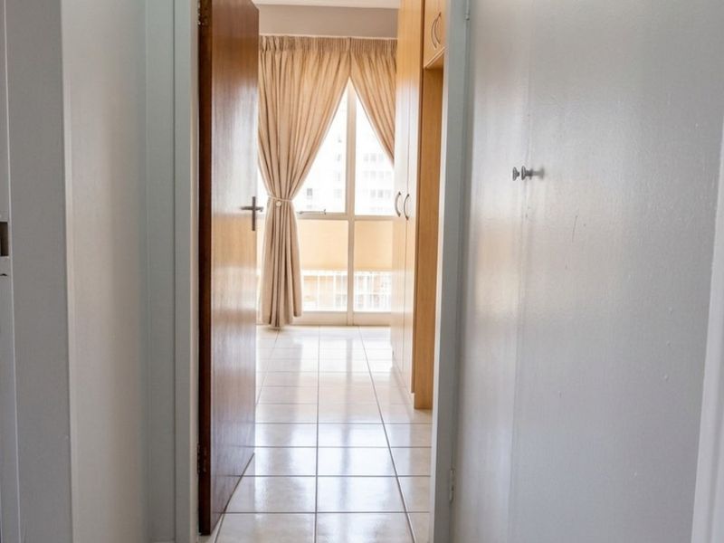 A clean, tiled hallway leading into a bedroom area featuring built-in storage cupboards and neutral wall finishes.