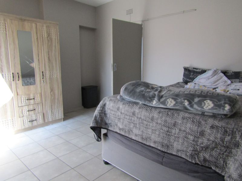 A bedroom featuring neutral wall tones, tiled flooring, and a built-in wardrobe, offering a functional and clean living space.