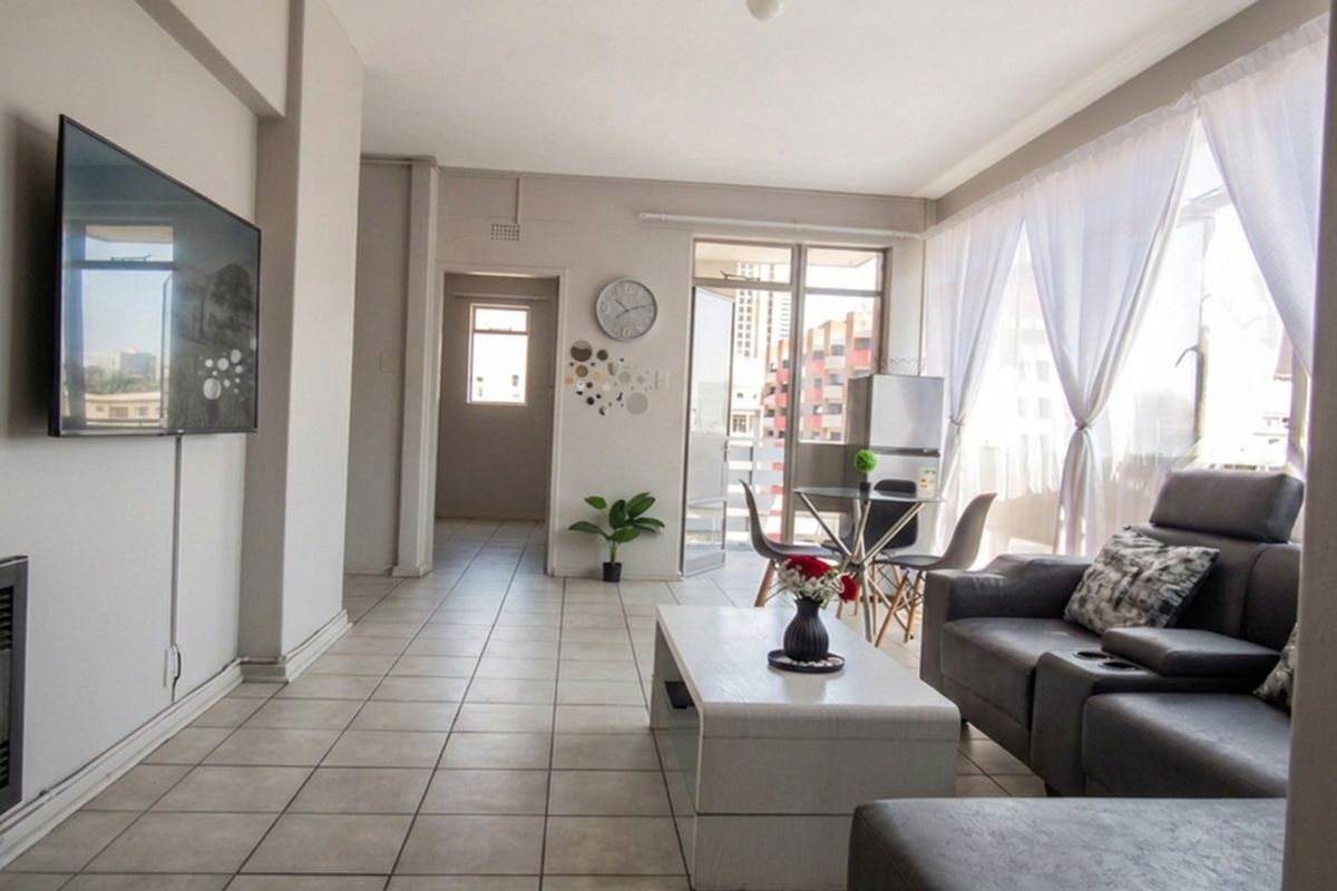 A bright living room featuring neutral tiled flooring, coved ceilings, and a sliding glass door providing access to an outdoor balcony area.