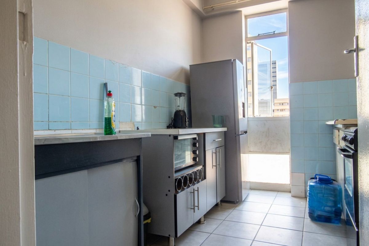 A functional kitchen featuring tiled splashbacks, built-in cabinetry, and tiled flooring, with natural light provided by a large window.