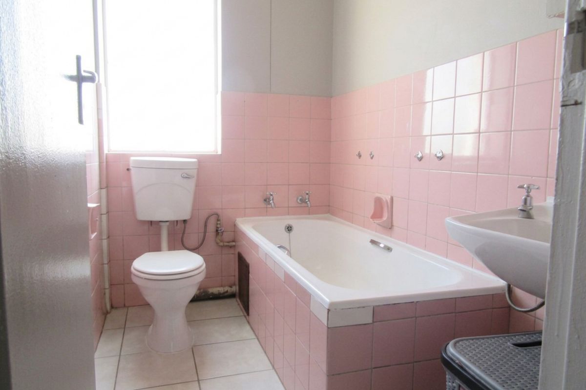 A dated bathroom featuring original pink wall tiles, a standard bathtub, pedestal basin, and toilet, offering significant potential for a modern renovation.