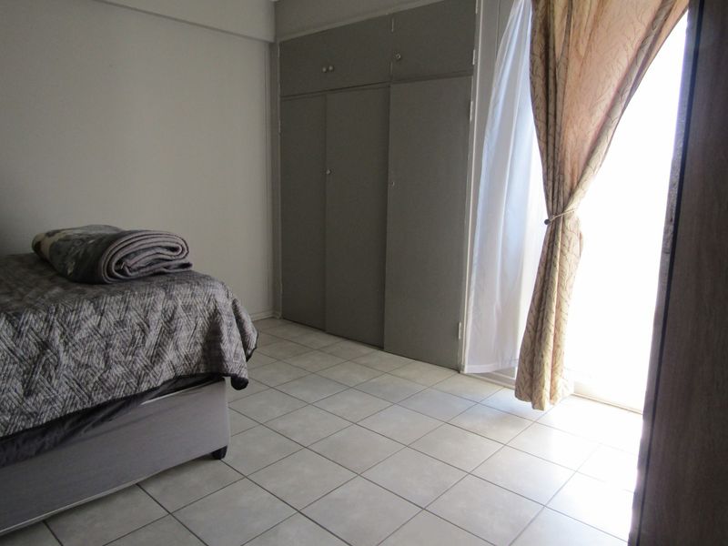 A bedroom featuring tiled flooring, built-in cupboards, and a sliding door providing access to natural light.
