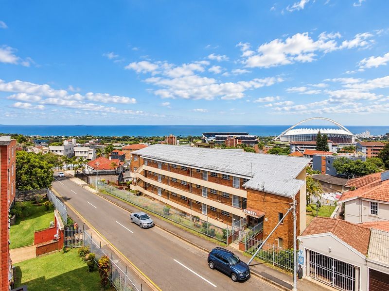 Aerial view of the apartment complex featuring brick construction, corrugated roofing, and external access staircases, situated in a coastal urban neighborhood.