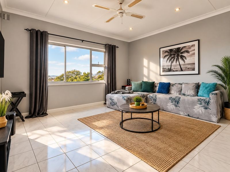 A bright and well-maintained living room featuring neutral tiled flooring, recessed downlighting, a ceiling fan, and large windows providing natural light.