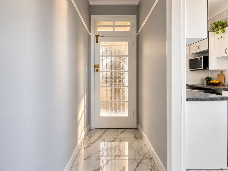 A bright, modern hallway featuring polished marble-look floor tiles and a classic glass-panelled entrance door with a transom window.