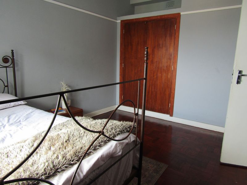 A bedroom featuring classic parquet flooring, a built-in wooden wardrobe, and neutral wall tones with a traditional picture rail.