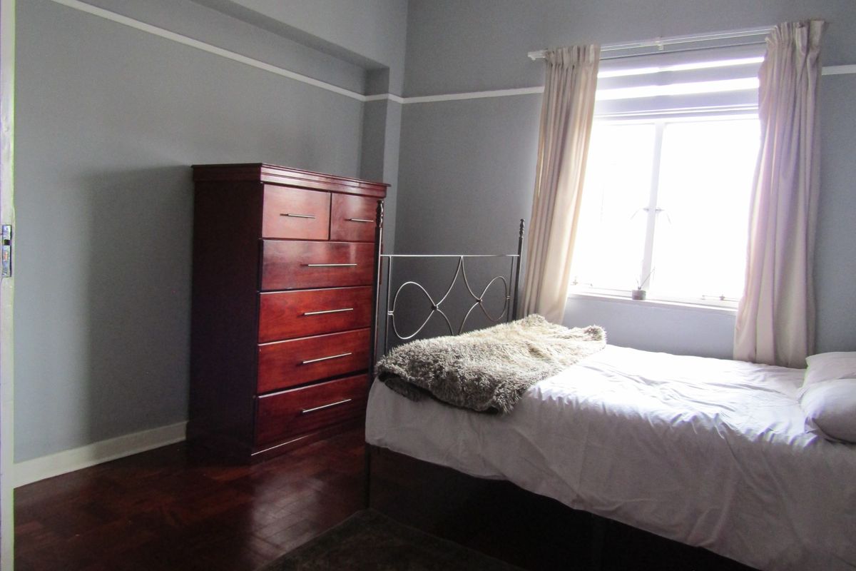 A bedroom featuring dark parquet flooring, grey walls with picture rails, and a window providing natural light.