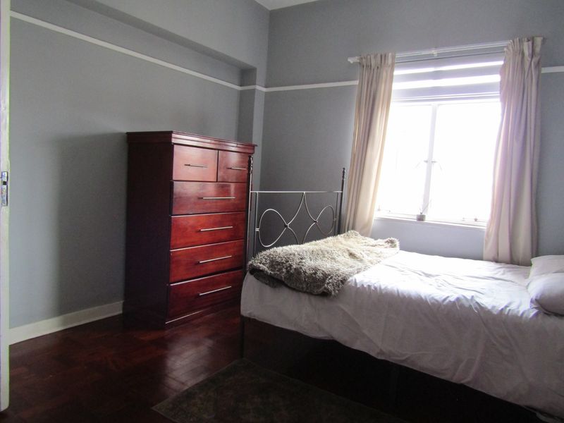 A bedroom featuring dark parquet flooring, grey walls with picture rails, and a window providing natural light.