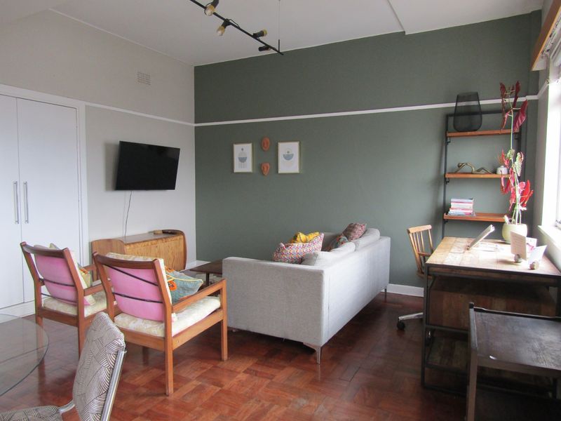 A well-maintained living room featuring classic parquet flooring, a built-in cupboard, and a feature wall with picture rail detailing.