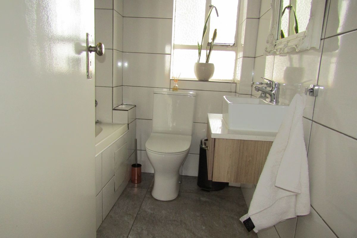A compact, modern bathroom featuring a wall-mounted vanity, white basin, toilet, and a bathtub with tiled finishes throughout.