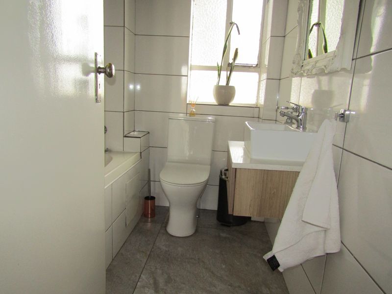 A compact, modern bathroom featuring a wall-mounted vanity, white basin, toilet, and a bathtub with tiled finishes throughout.