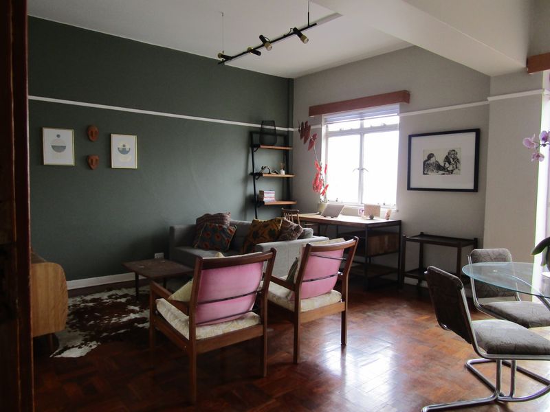 An open-plan living and dining area featuring original parquet flooring, a classic picture rail, and large casement windows providing natural light.
